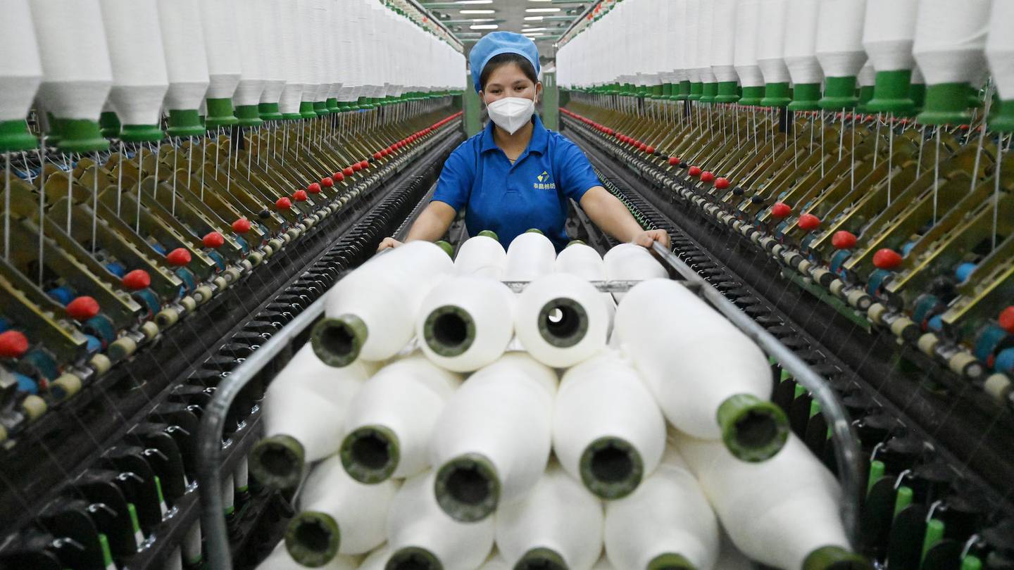An employee in a blue uniform pushes a trolley filled with spools of cotton yarn through a factory.