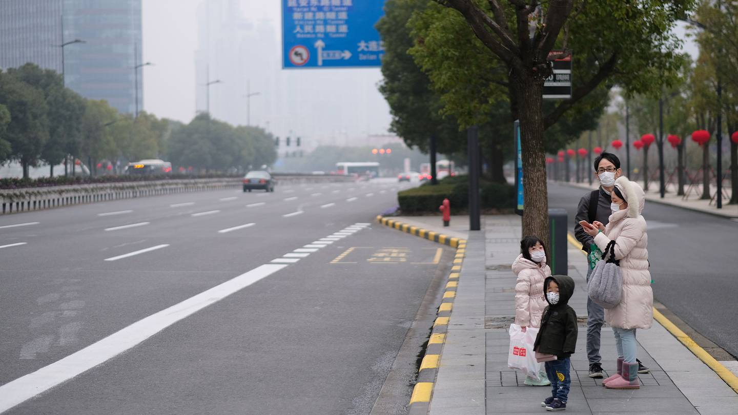 A family stand on the side of an empty road in China with face masks on.