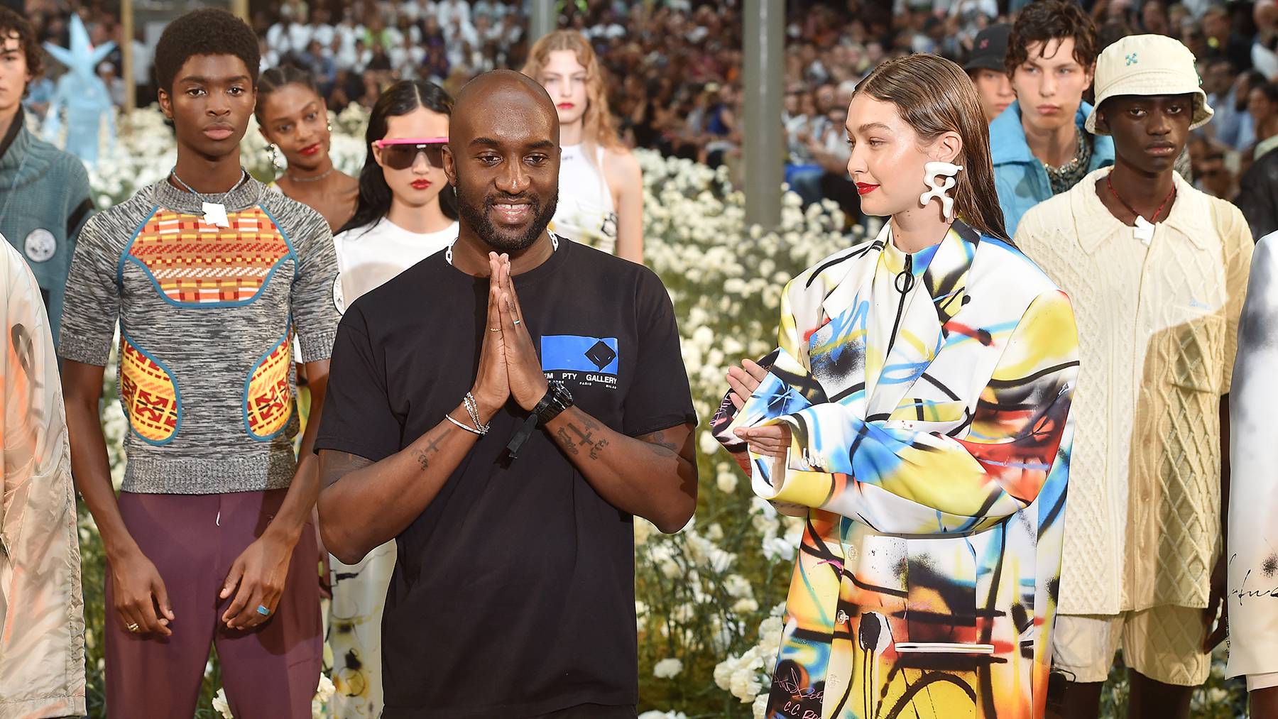 Virgil Abloh at the finale of a show standing in front of the models and beside Gigi Hadid.