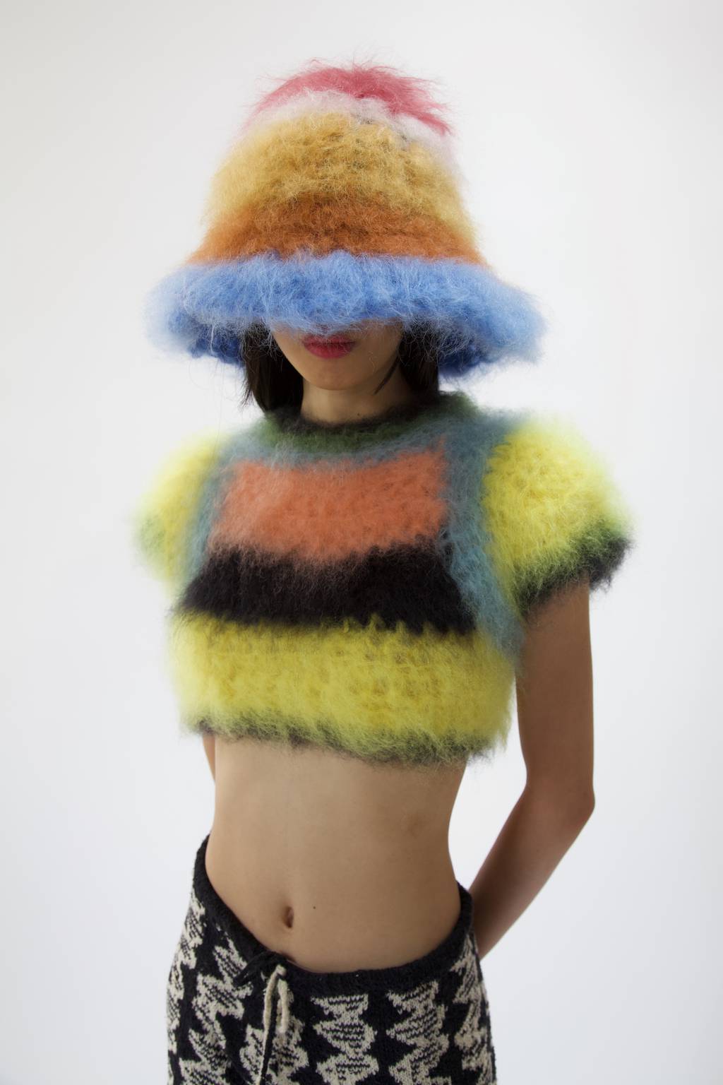 Women wearing a fuzzy knitwear hat and cropped jumper. Both brightly colour stripes.