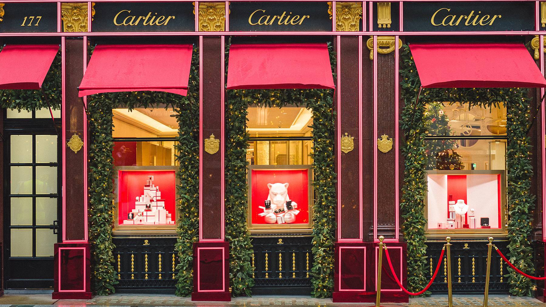 The exterior of a Cartier store showcasing jewels in the window display and the stores signage at the top.