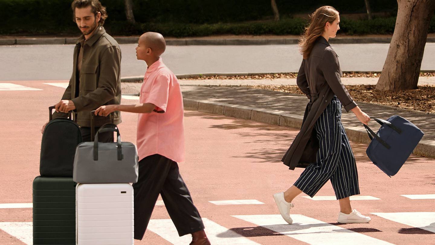 Three people crossing the street with Away Luggage and bags