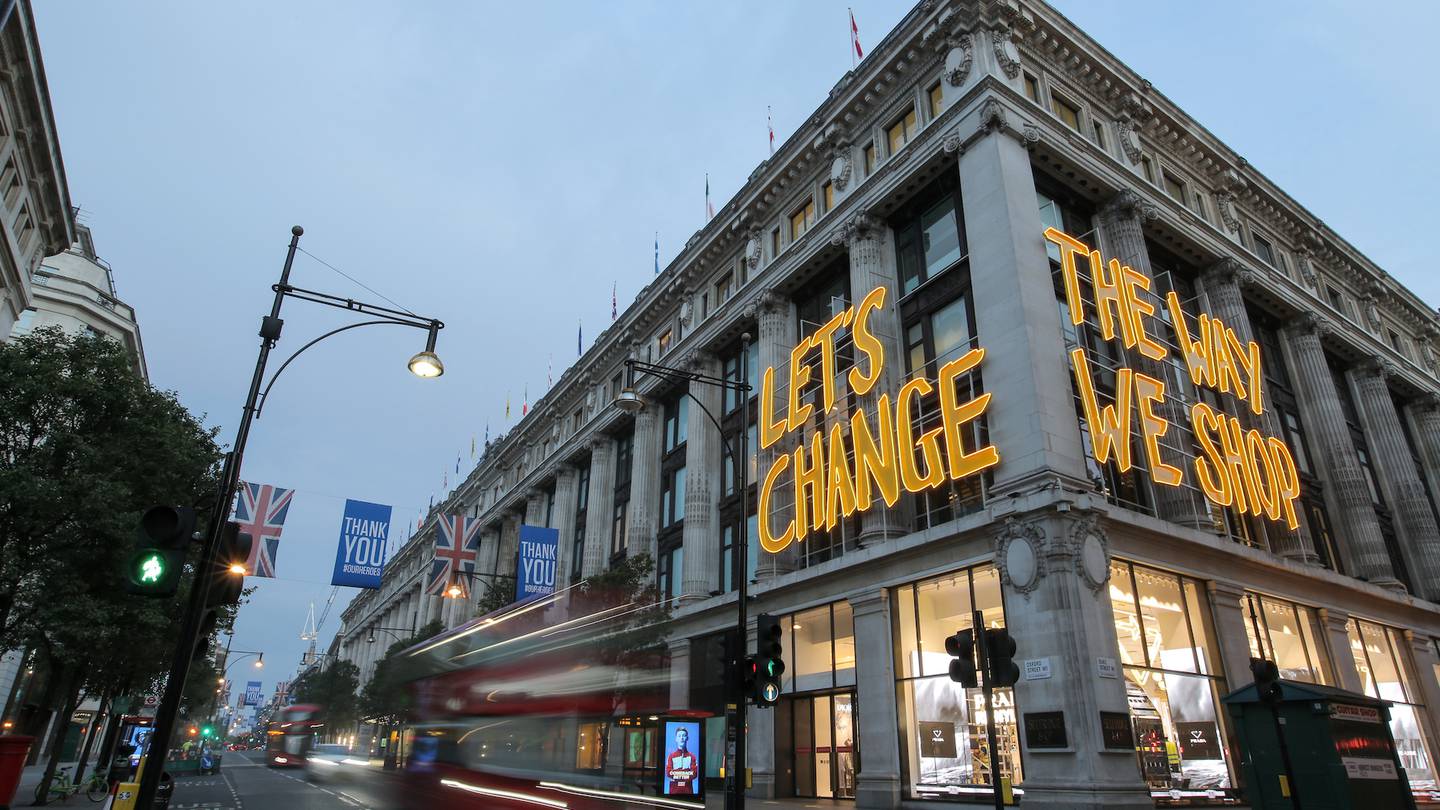 A sign lit up in yellow saying "let's change the way we shop" hangs on the facade of the Selfridges store on London's Oxford Street.