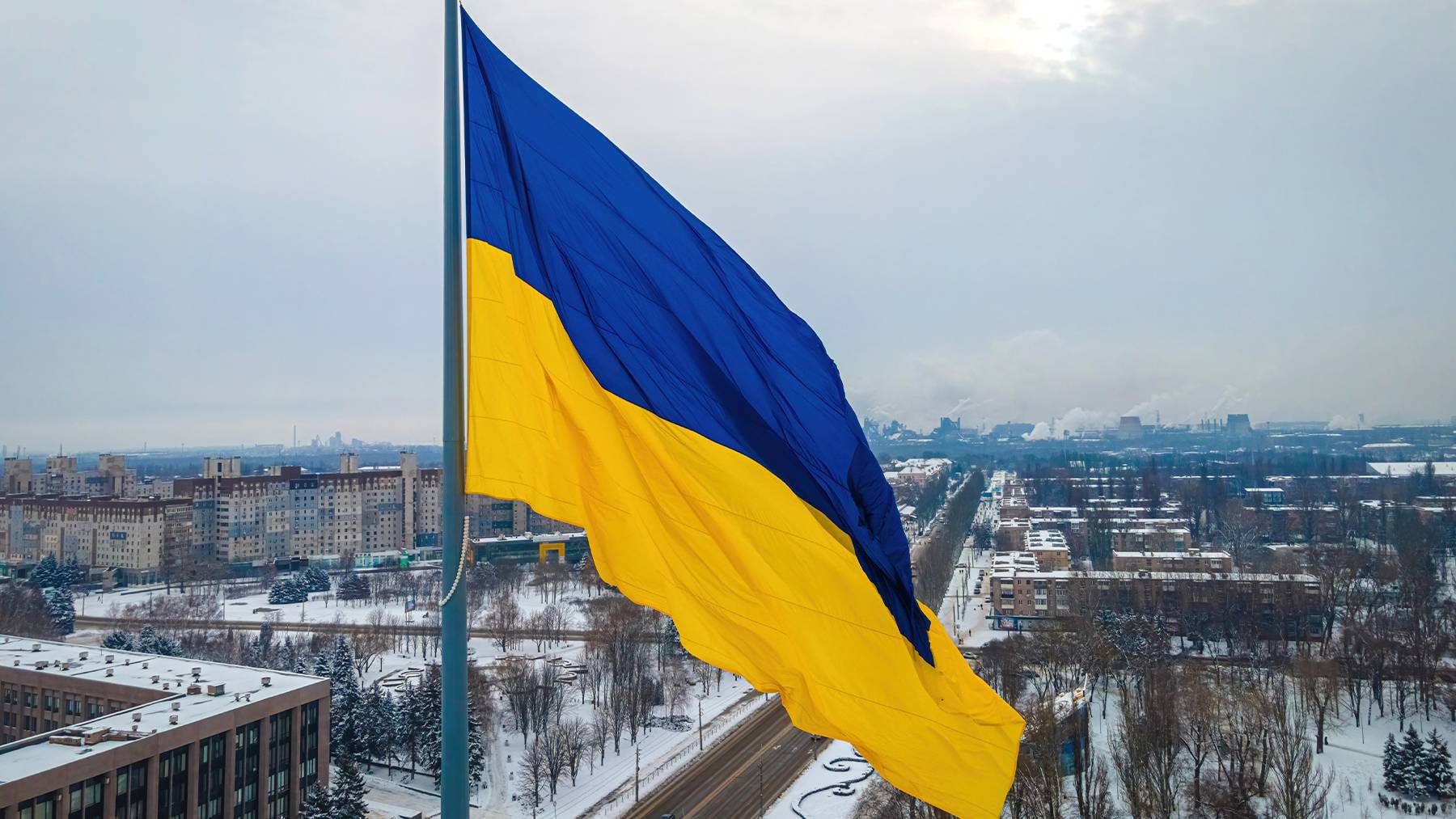 Ukraine's blue and yellow flag stands in the foreground against a backdrop of a snowy city.
