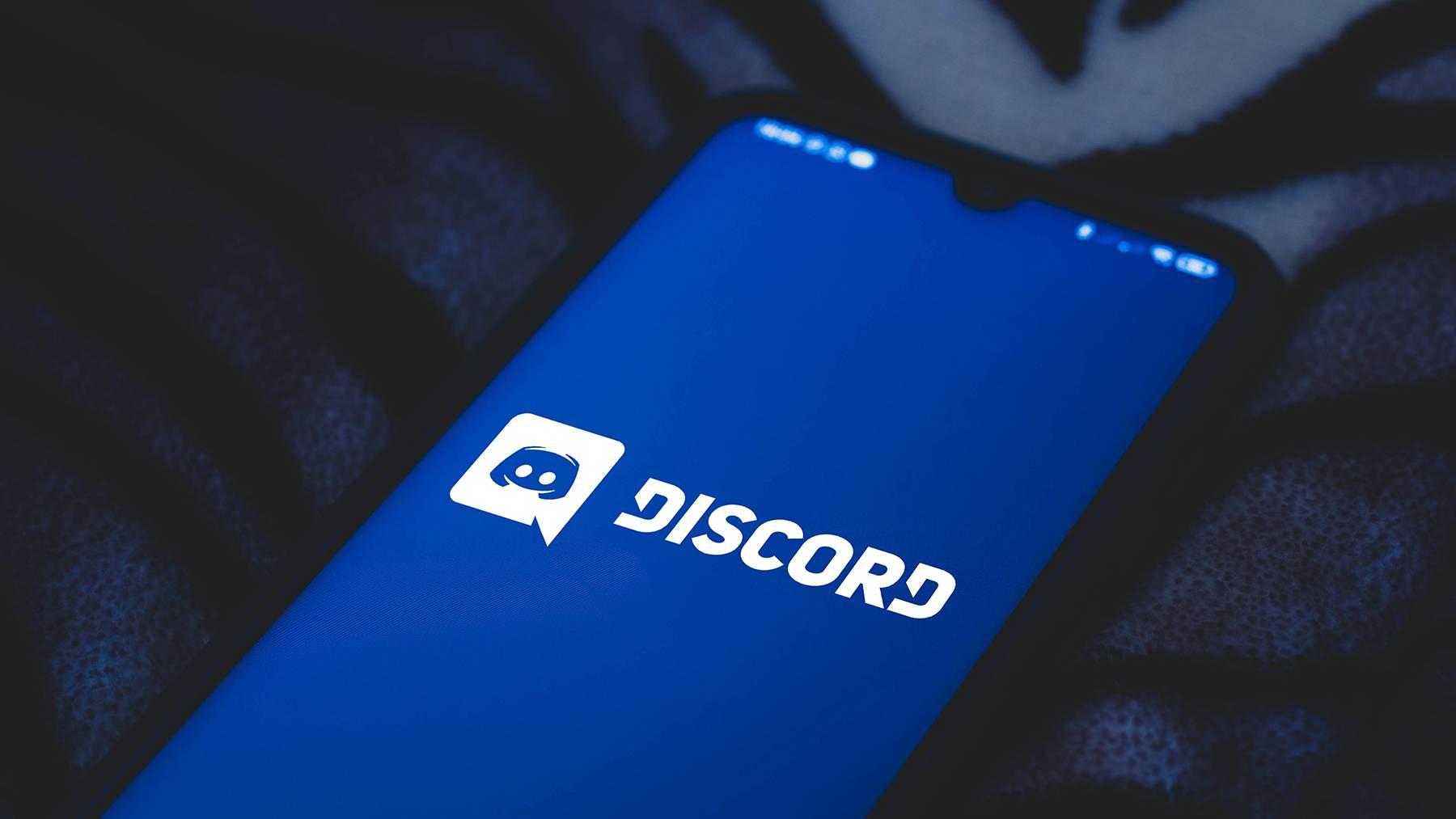 A mobile phone displays a screen with the Discord logo.