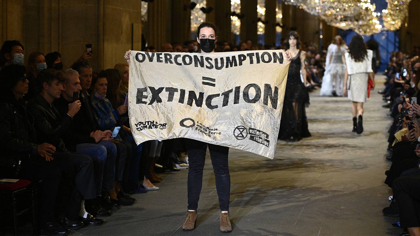 An Extinction Rebellion protestor holds a banner reading "OVERCONSUMPTION = EXTINCTION" on the runway of the Louis Vuitton Spring/Summer 2022 women's show.