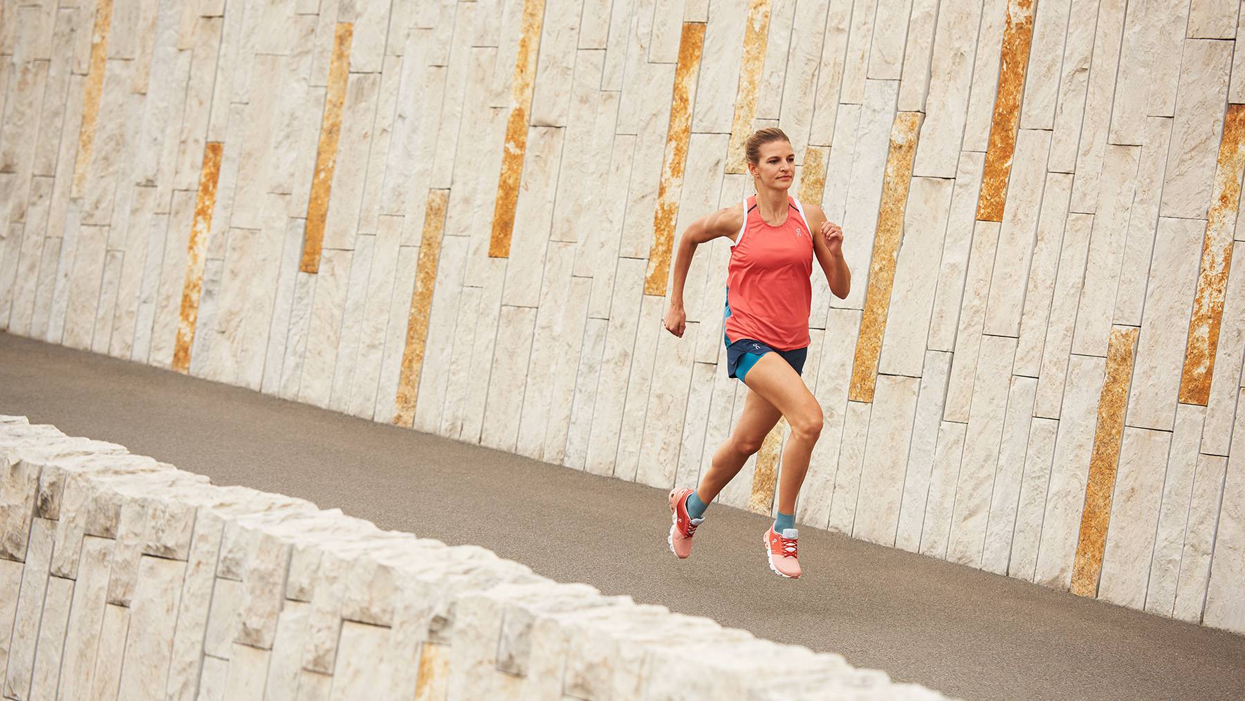 A woman wears red and white On trainers running along a concrete road.