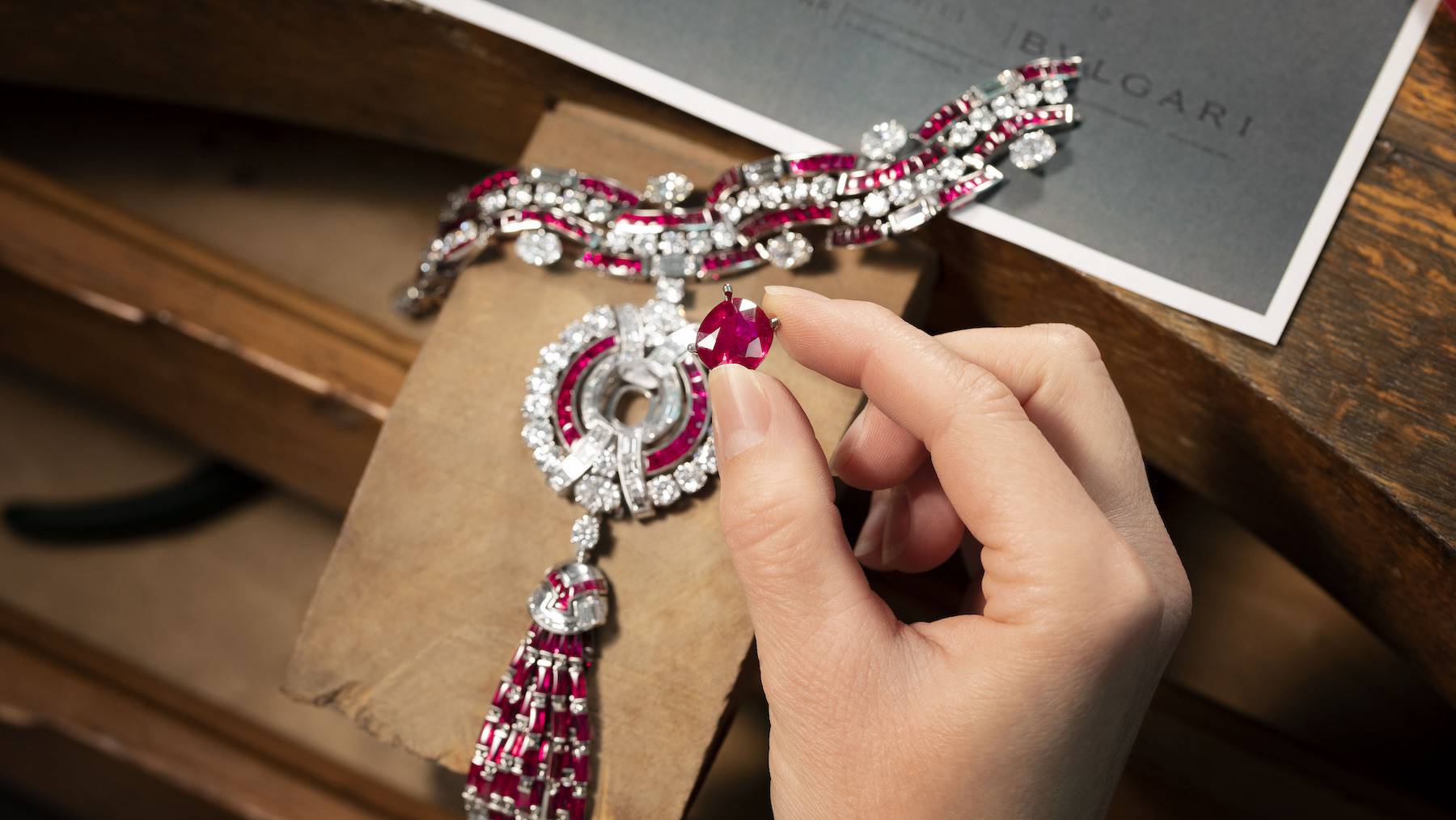A hand placing a jewel into a Bulgari necklace.