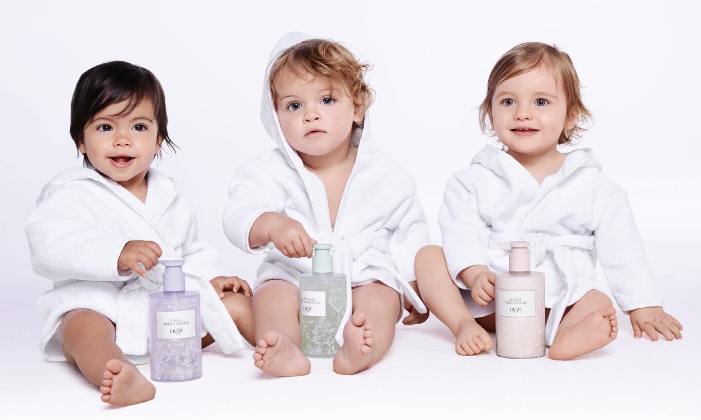 Babies in terrycloth robes with Dior skincare products.