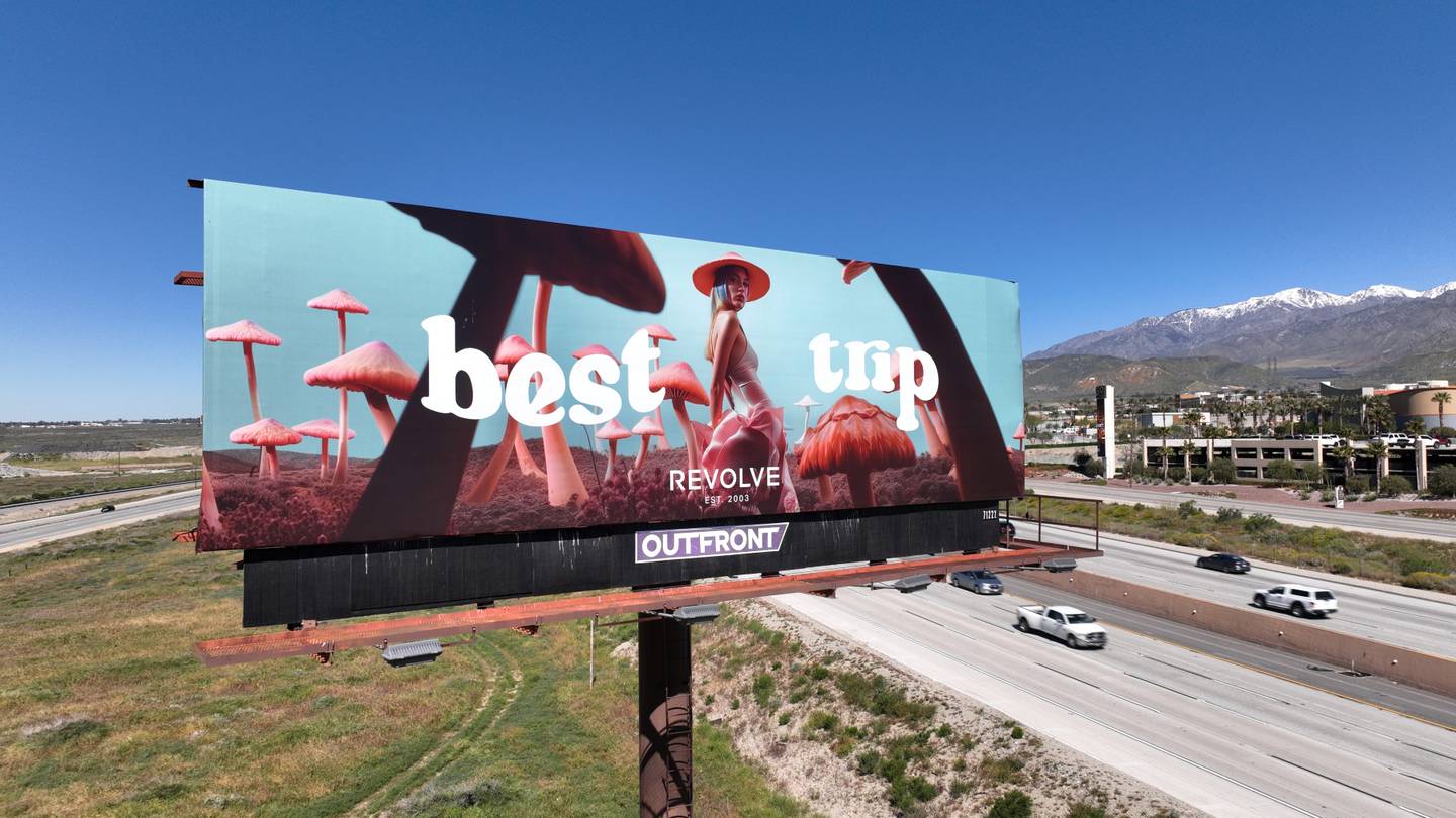 A billboard featuring an AI-generated image of a model amid giant mushrooms stands alongside a highway in California.