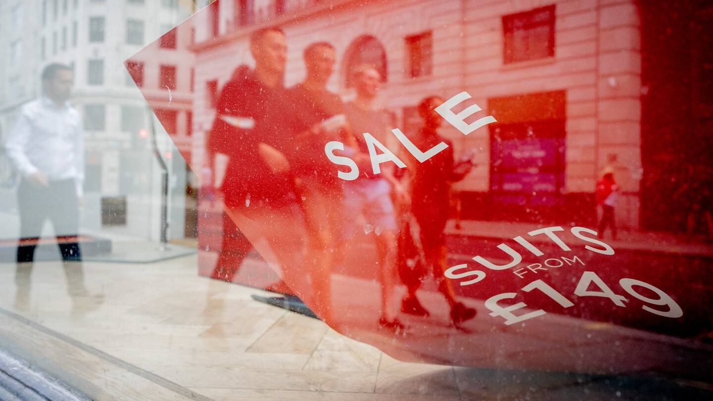 Male passers-by and a detail of a fallen sheet describing the sale of menswear suits, in a closed clothing business in the City of London.