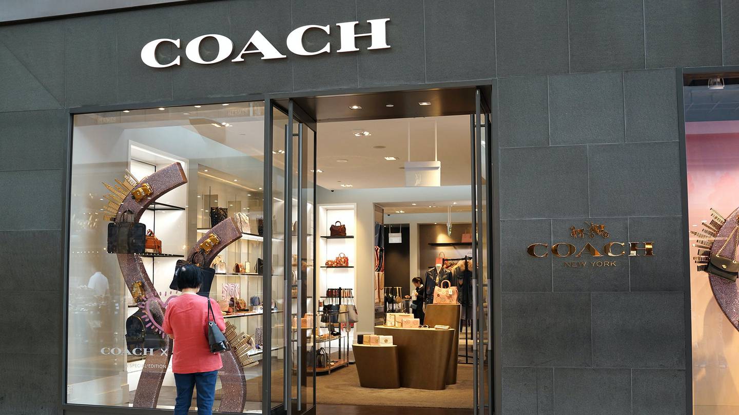 The exterior of a Coach store with a shopper window shopping bags outside the store.