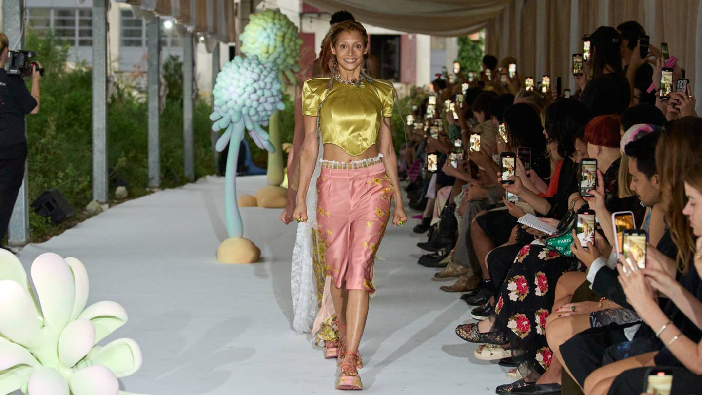 A model in a gold top and pink shorts walks the runway at Collina Strada.