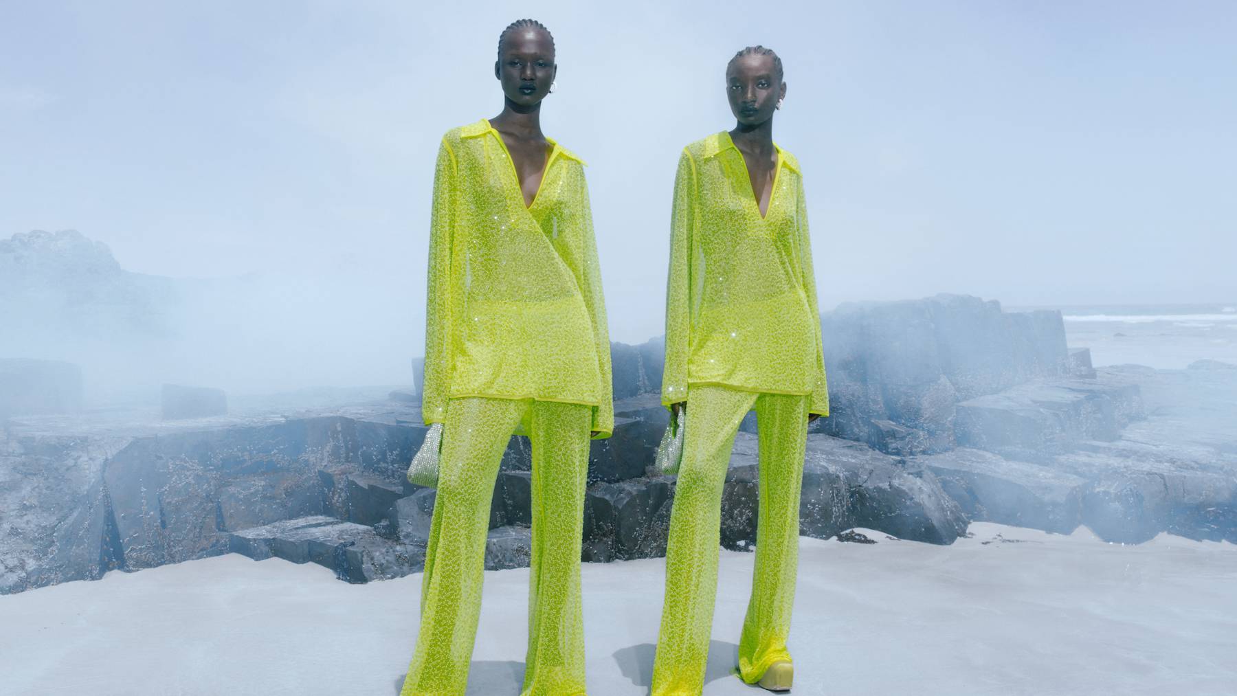 Two models in draped lime-green sequinned suits by H&M stand against a misty backdrop.