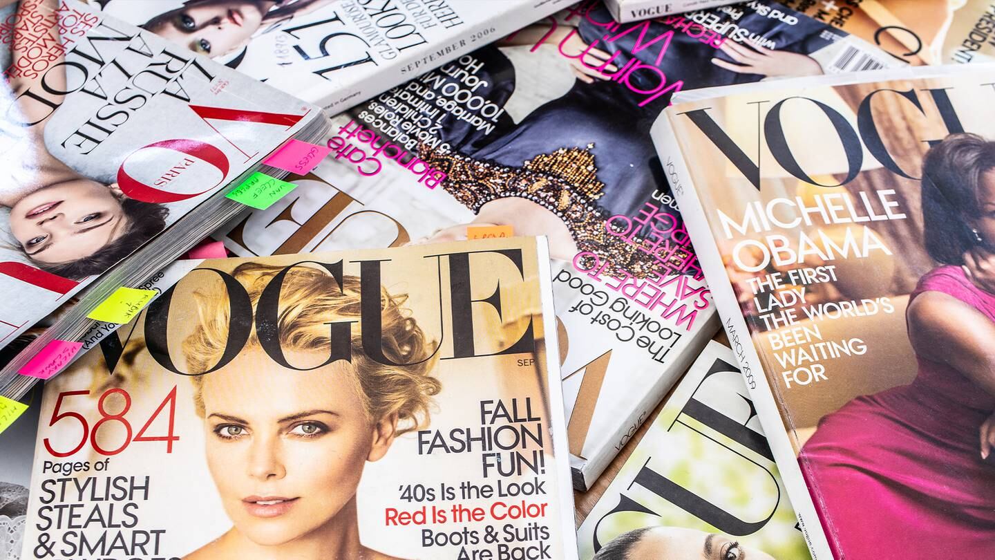 A pile of Vogue magazines covers spread over a table.