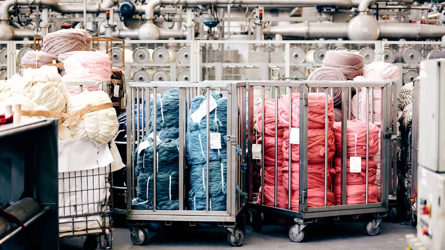 Crates of dyed yarn in different colours stand before machinery in a dyeing factory.