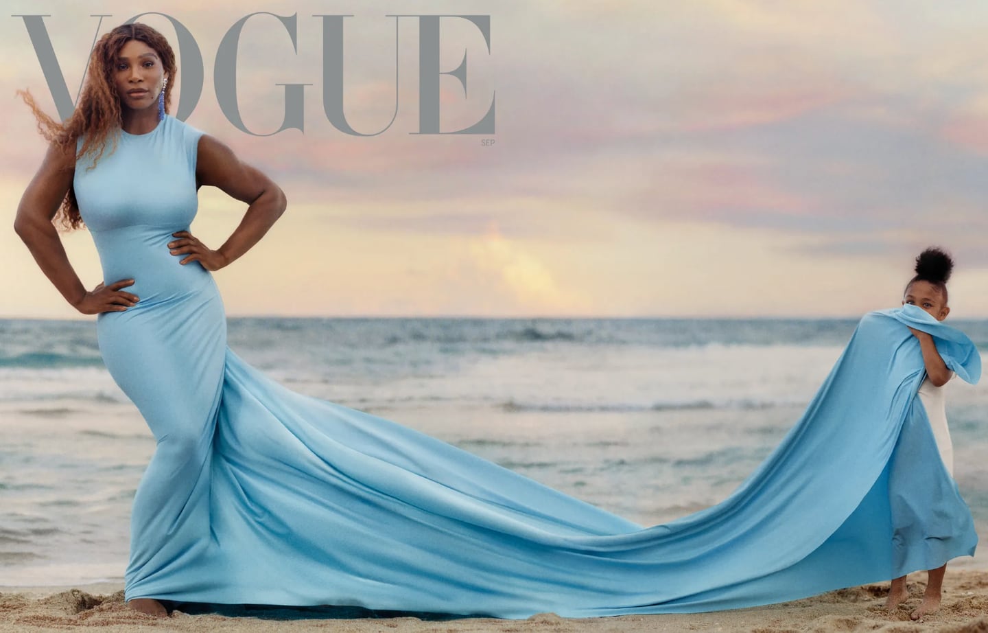 Serena Williams stars on the front cover of Vogue's September 2022 issue. She wears a blue gown with a long train held by her daughter on a beach, in front of a sunset.