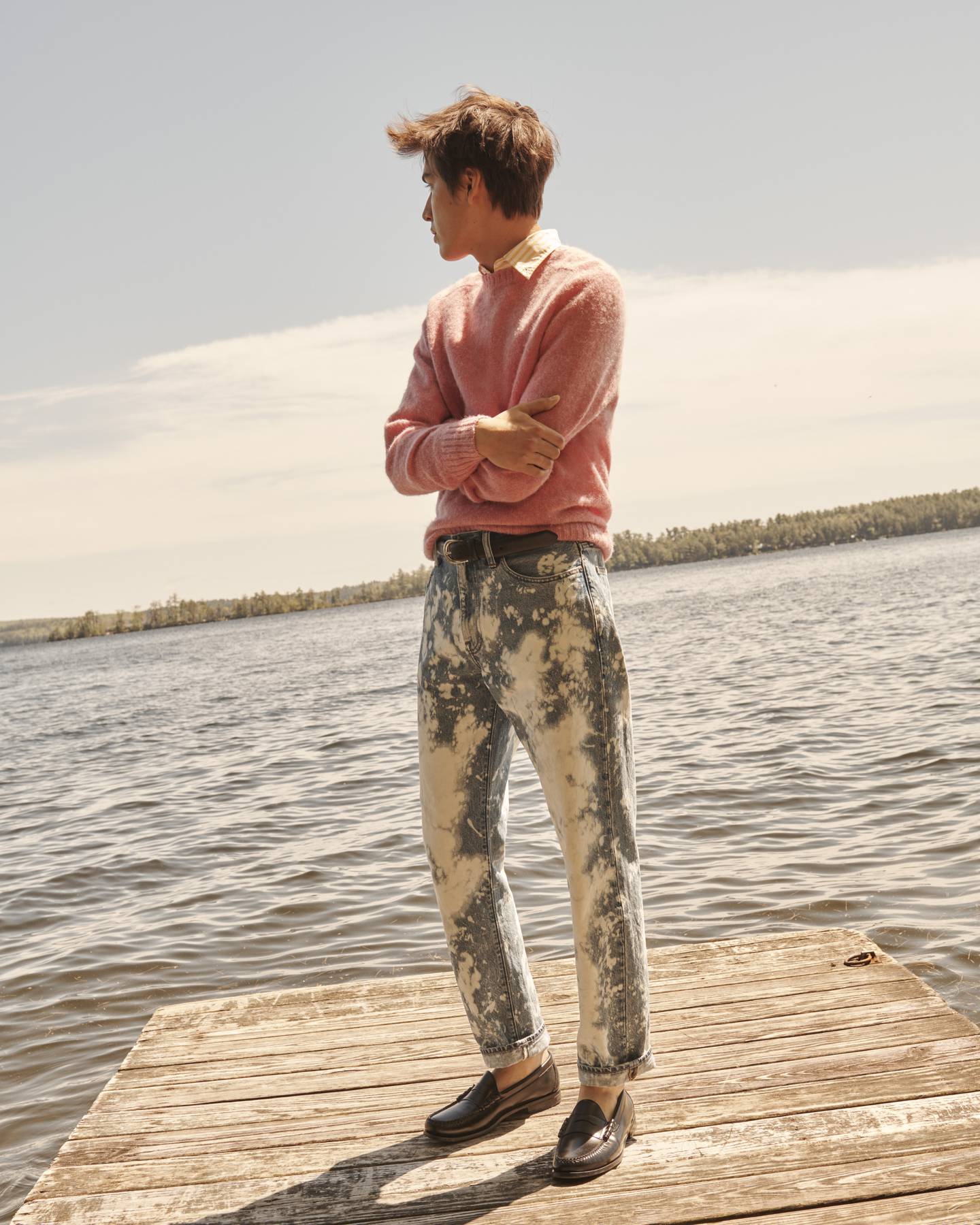 Blond model wearing acid wash jeans standing on dock in front of lake.