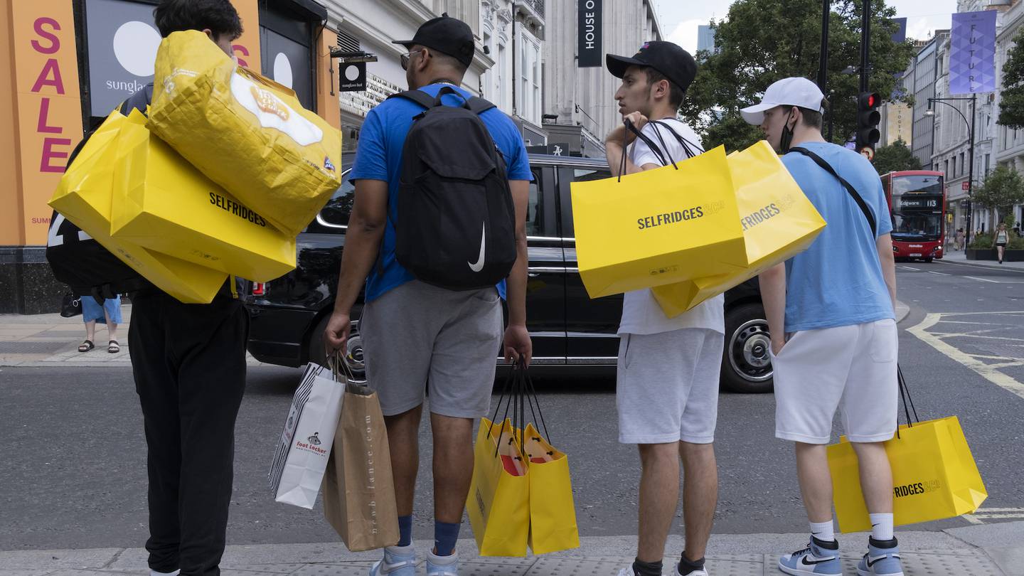 Young Men carry a shopping haul in yellow bags from British department store Selfridges.