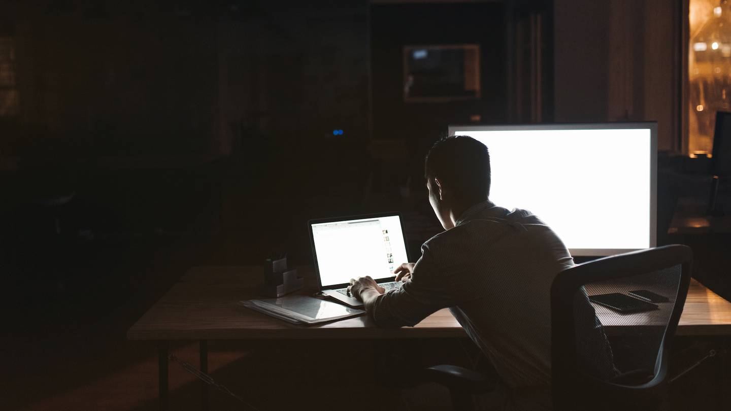 An employee working late at night, sat in front of two computer screens.