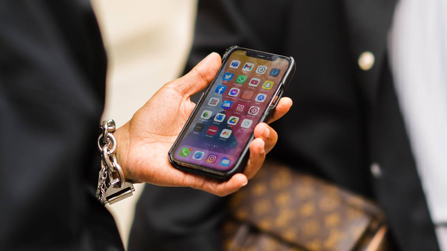 A man at Paris Fashion Week with a large silver bracelet holds his unlocked phone displaying several apps.