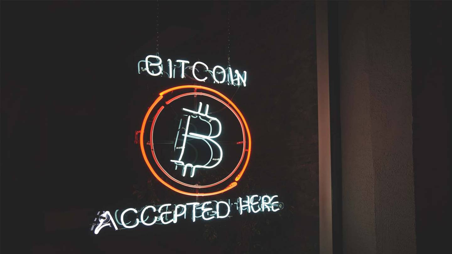 A neon sign in a shop window announces that Bitcoin is accepted there.
