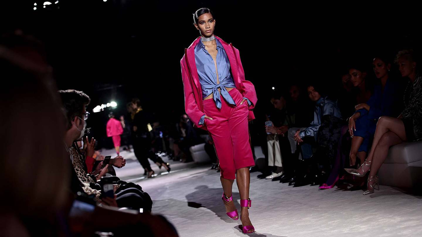 A model walks the runway at Tom Ford's Spring/Summer 2022 show in New York. She wears a blue shirt with a hot pink jacket and cropped trousers with matching pink heels.