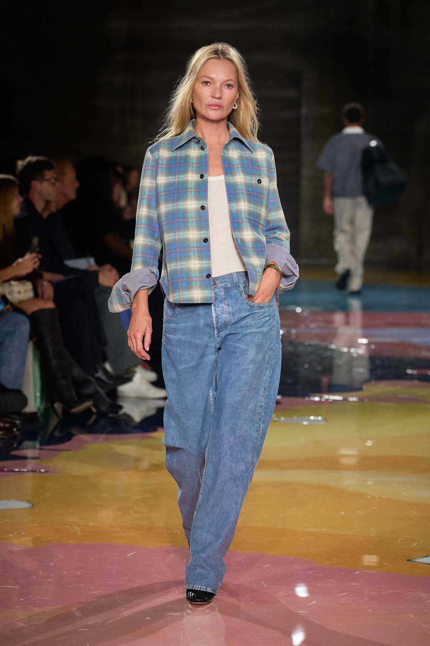 Kate Moss walks the runway wearing jeans and a blue plaid shirt over a white T-shirt, all made of leather, on the runway.