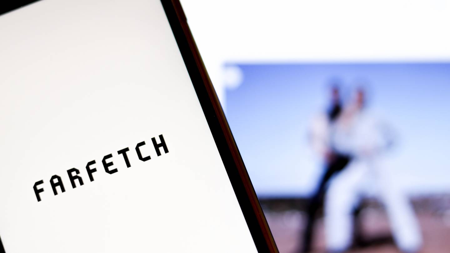 A shot of the Farfetch logo on a white background with blurred images of models in the background.