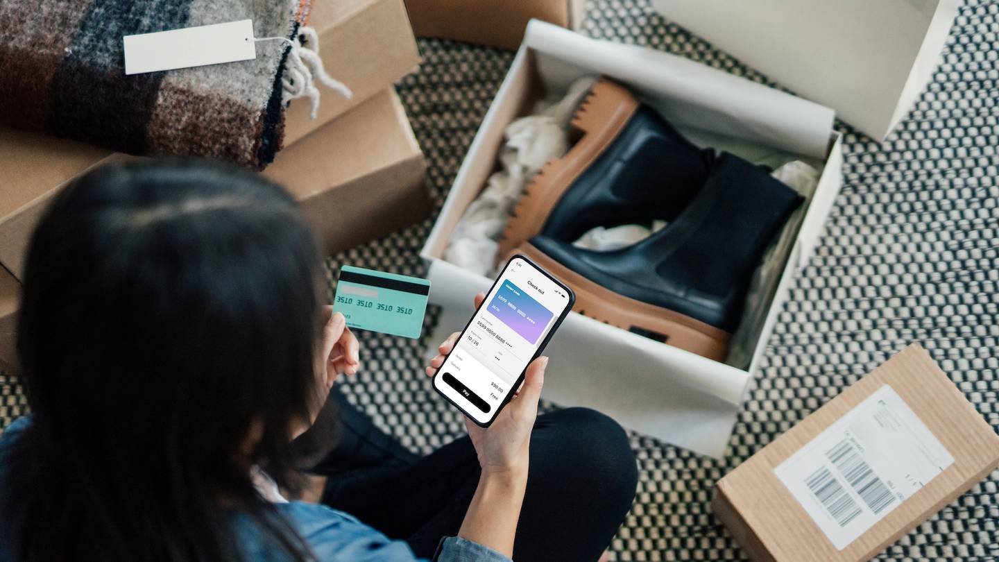 An online shopper uses their smartphone to purchase items. A box of new boots sits open in front of them.