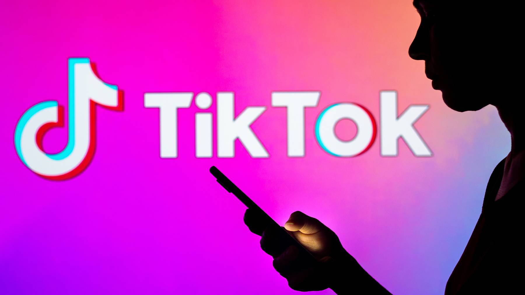The dark silhouette of a person looking into their phone stands out against a brightly coloured background with TikTok's logo.
