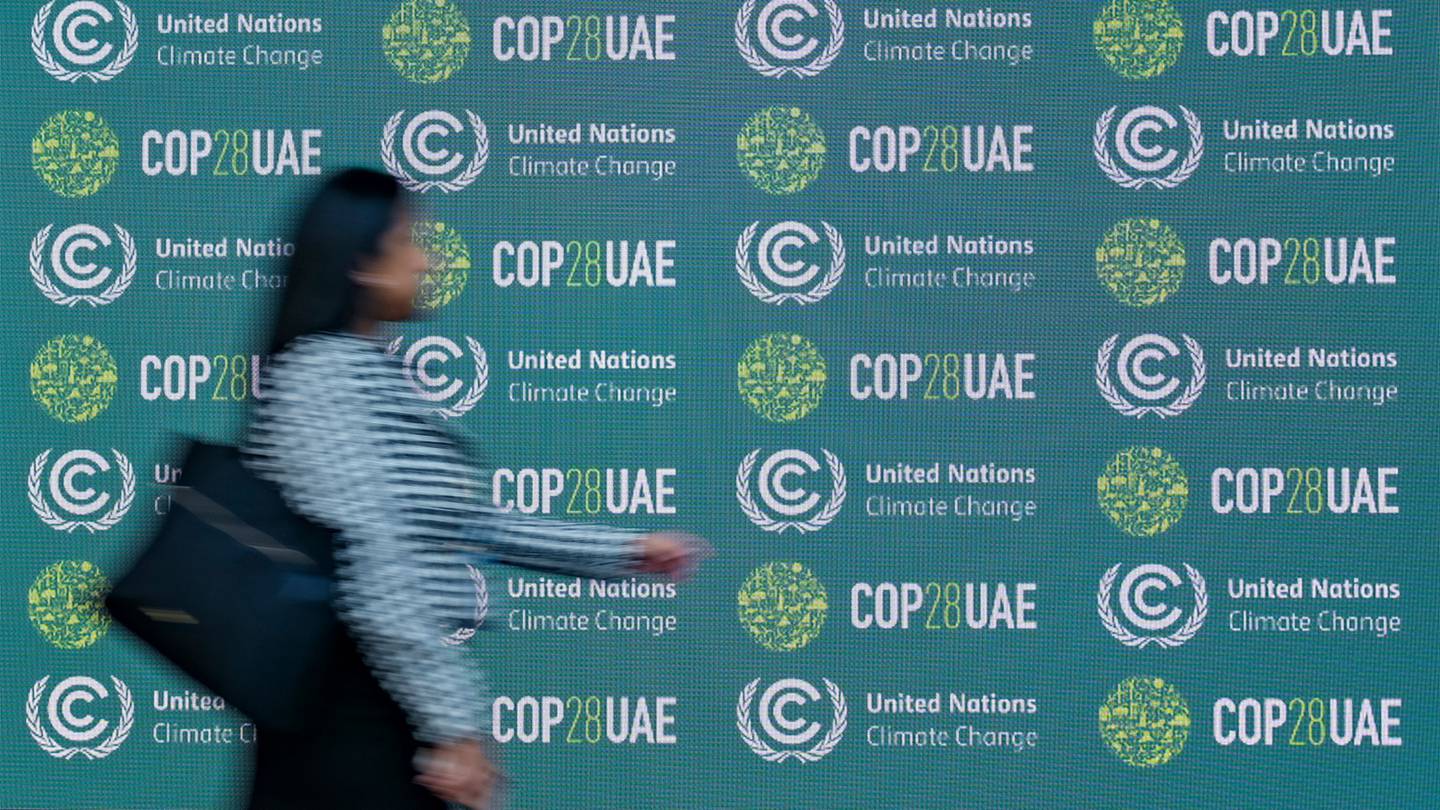 A woman walks by a board covered with signs for COP28 during a conference.