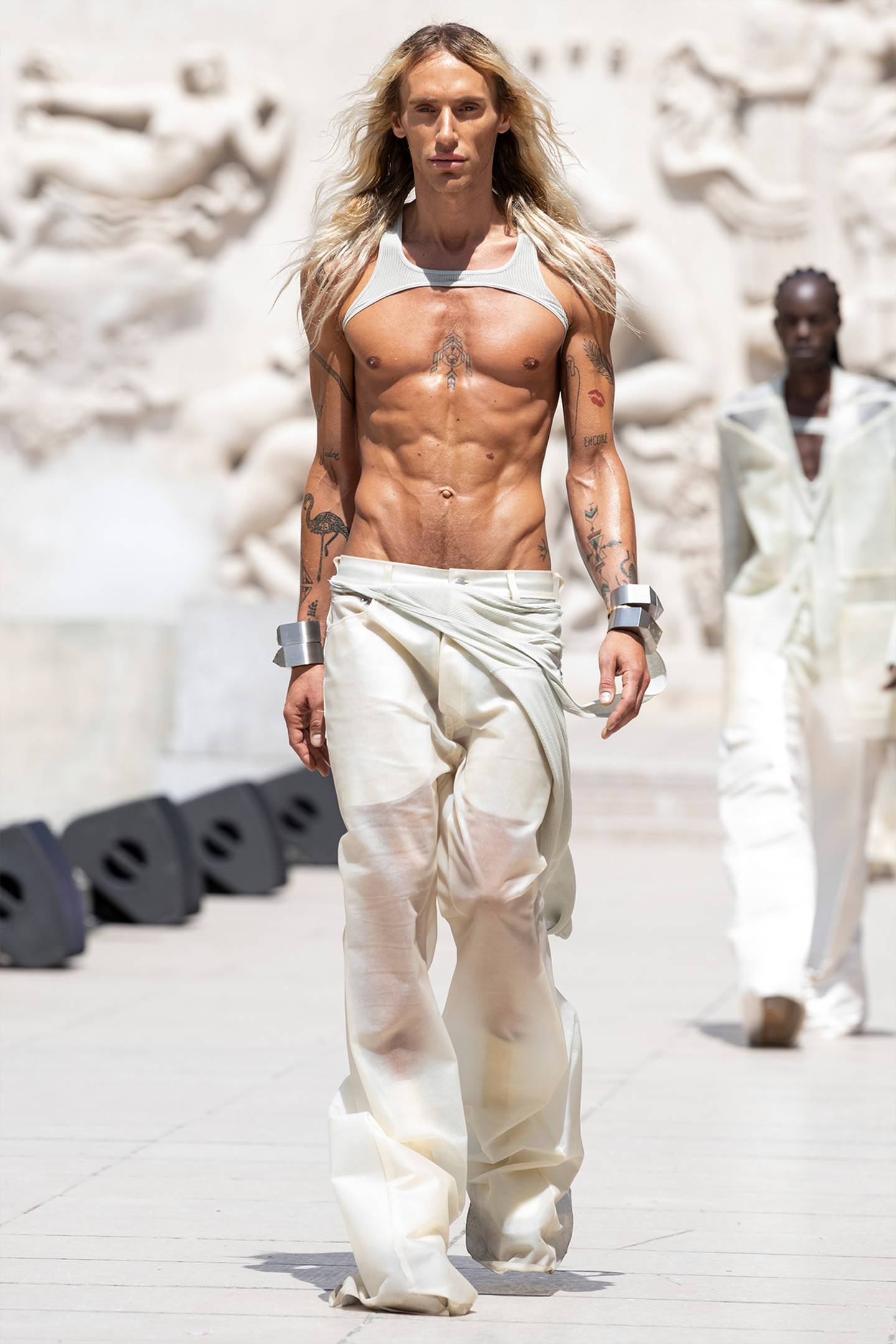 A model wears white trousers with a white body harness.