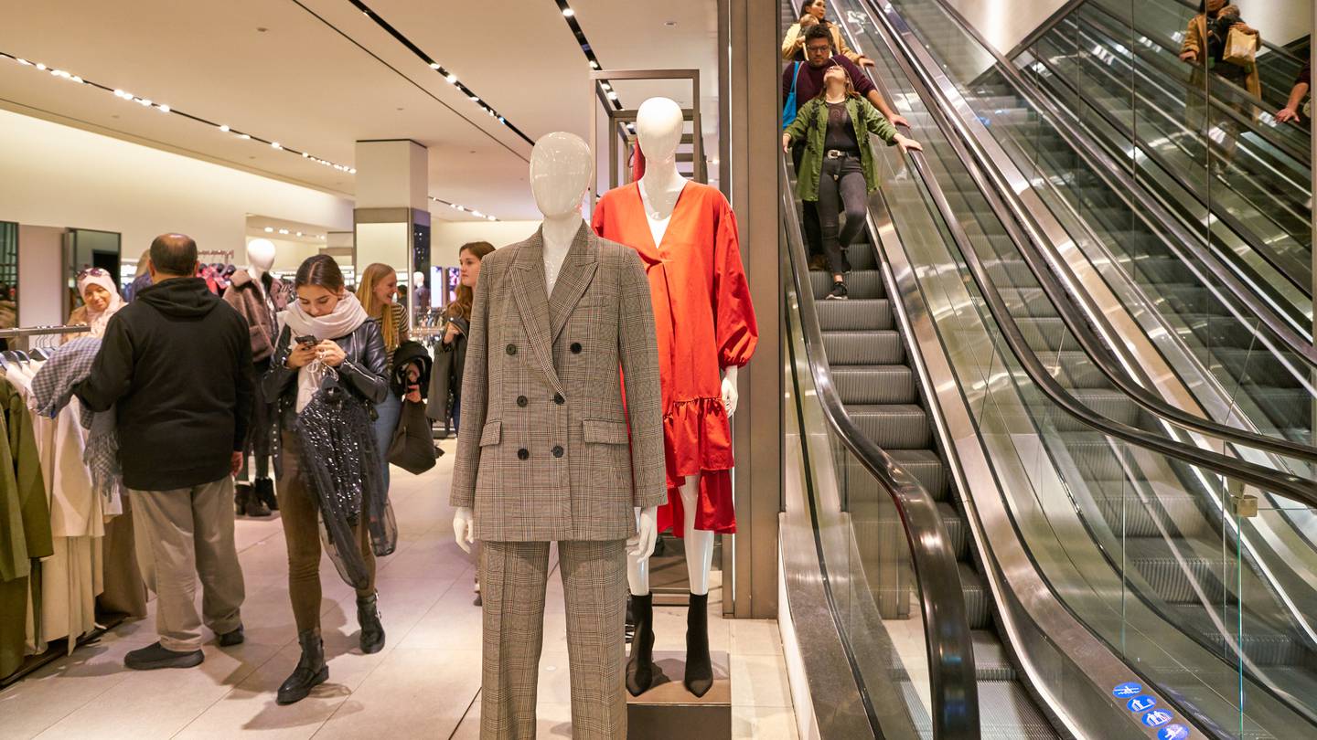 Mannequins stand in the foreground of a photograph of a store interior.