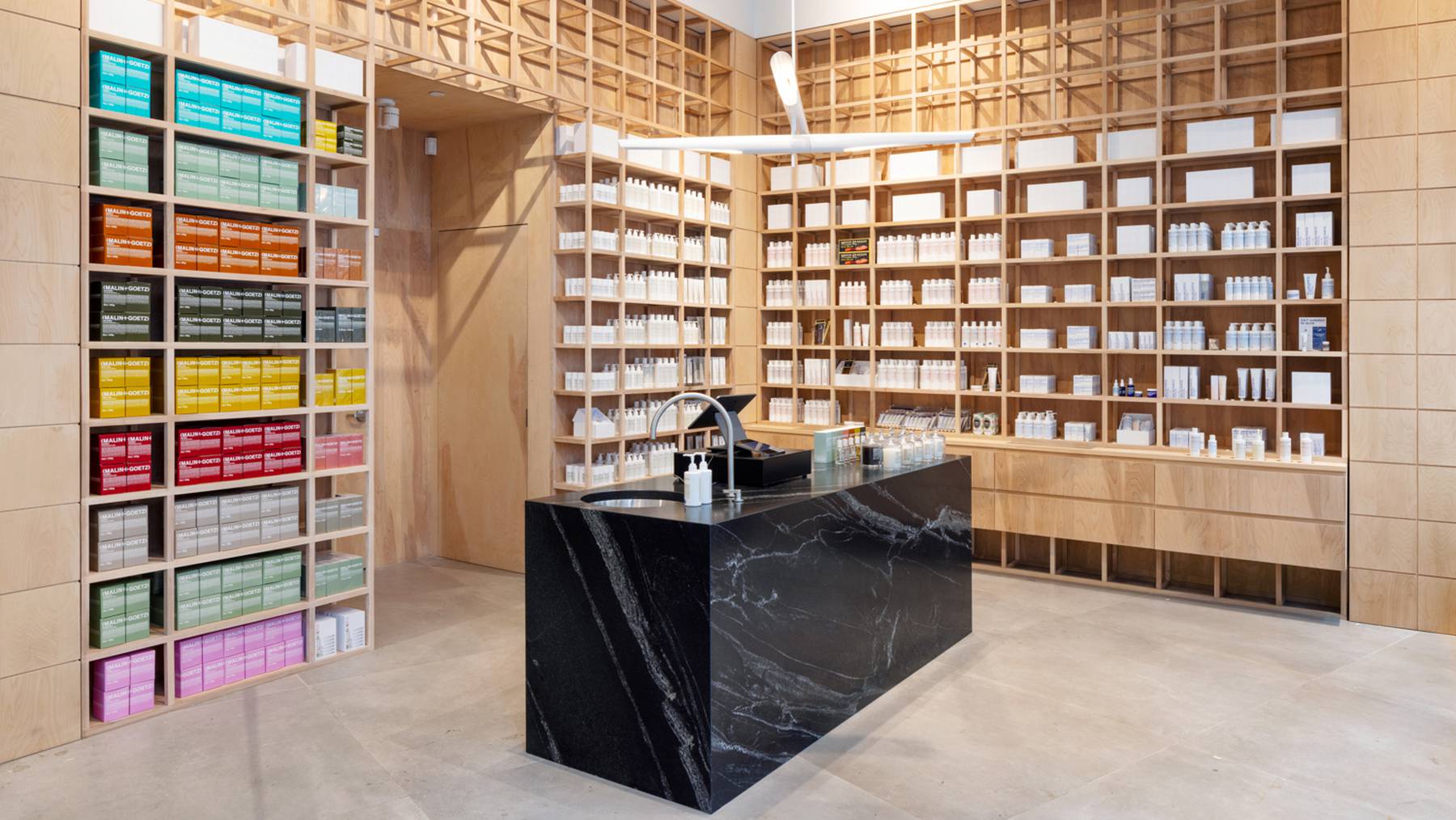A Malin+Goetz store with colourful products on wooden shelves.
