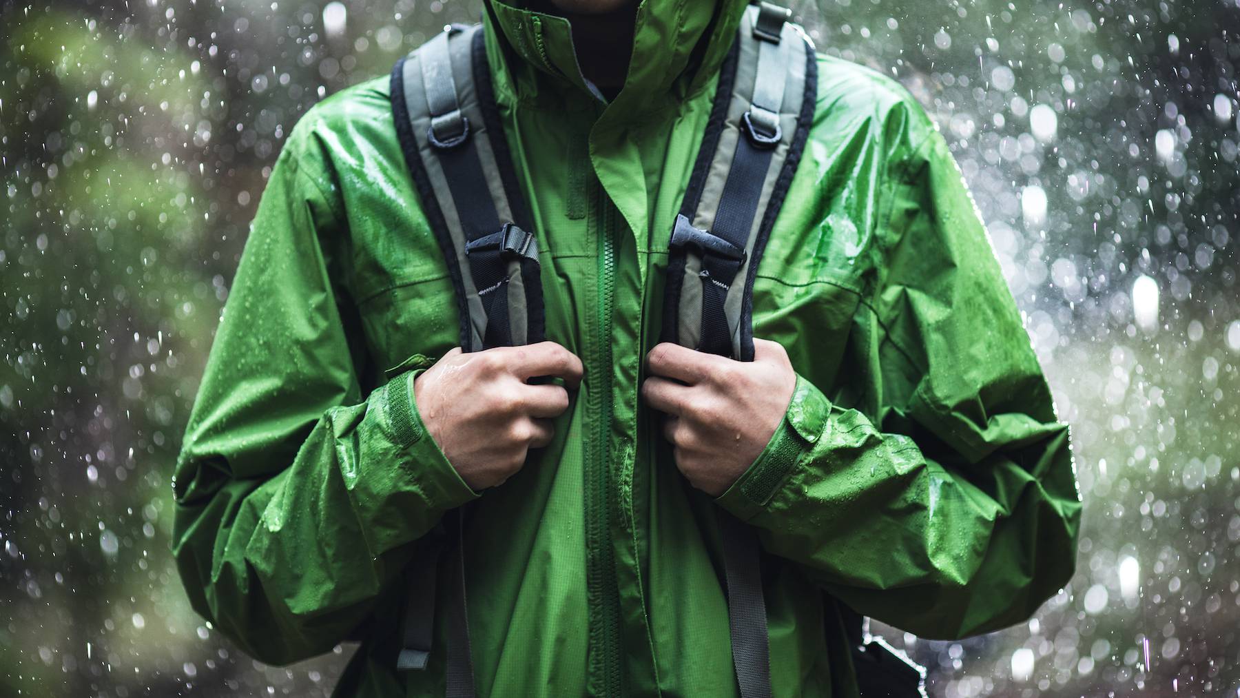 A man wearing a green waterproof jacket and grey backpack in the rain.