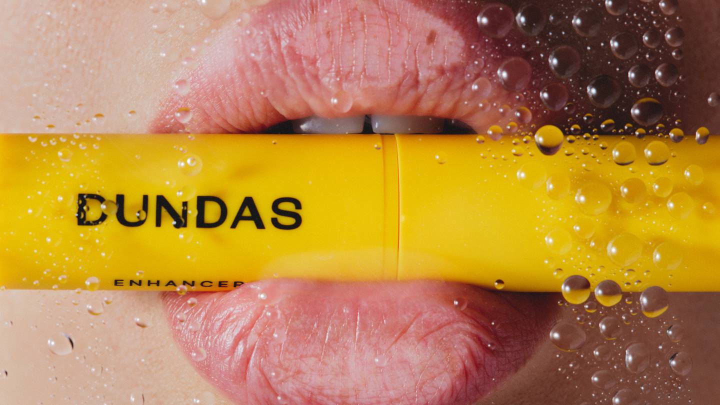 Lips holding a yellow tube of Dundas Beauty's new Pumped Lip Moisture balm.
