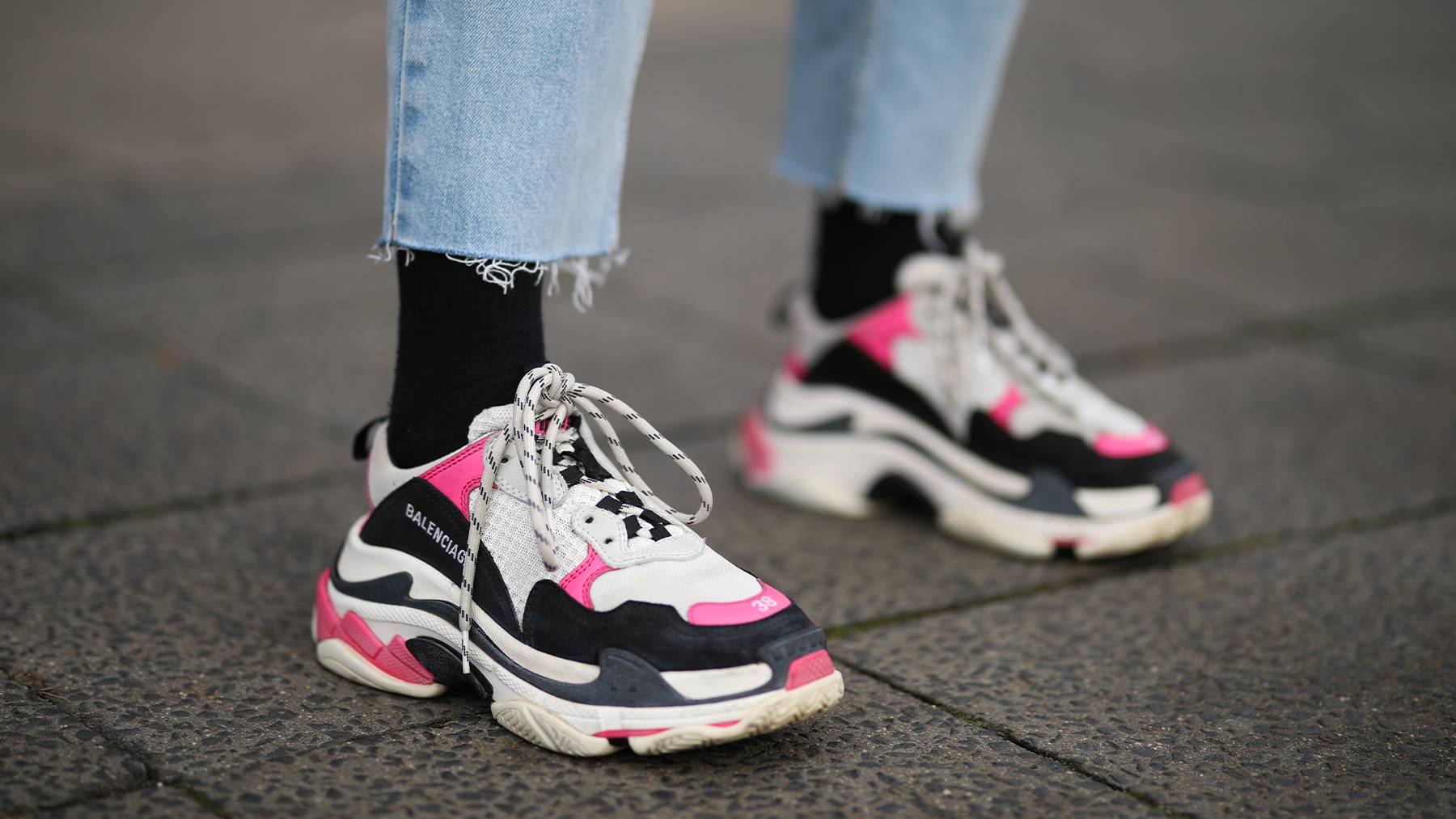 A close up view of white, black and pink Balenciaga chunky trainers worn with blue jeans.