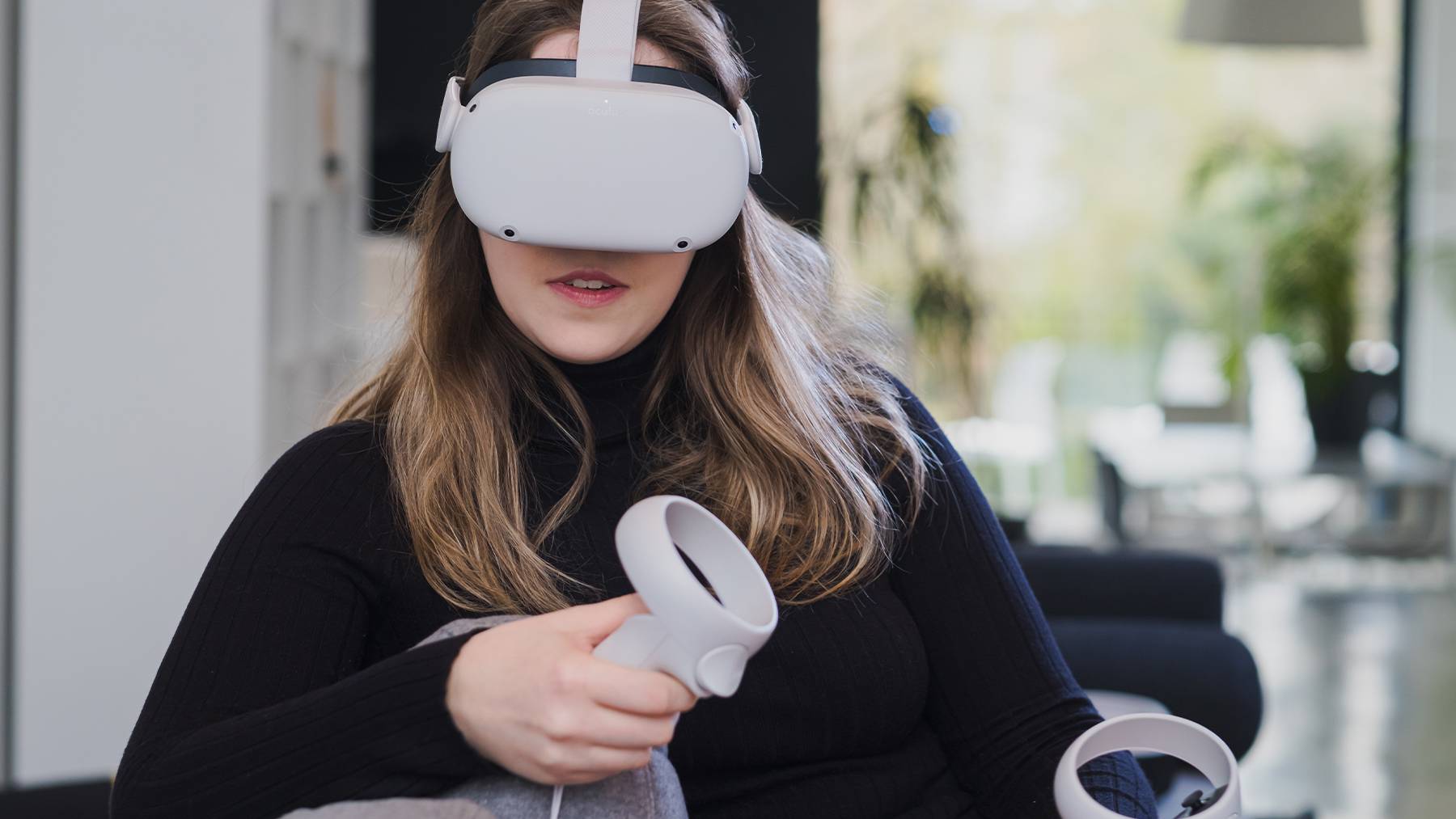 A woman in a black sweater wears a VR headset that covers her eyes.