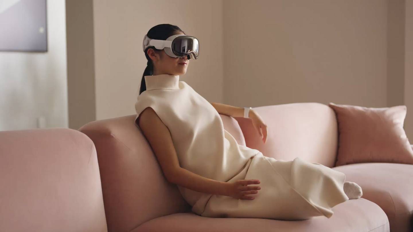 A woman sits on a couch wearing Apple's Vision Pro headset.