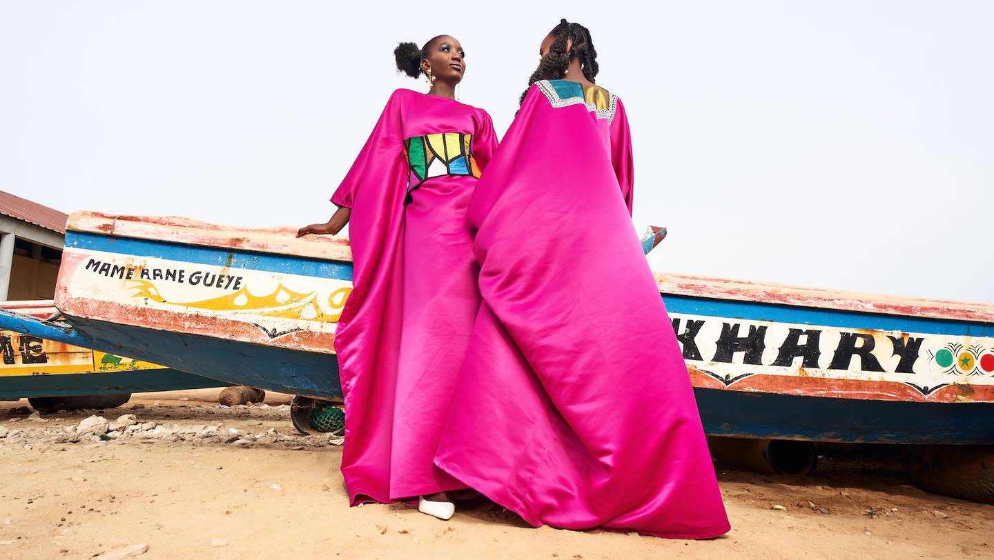 Two models pose in pink gowns in front of a boat.
