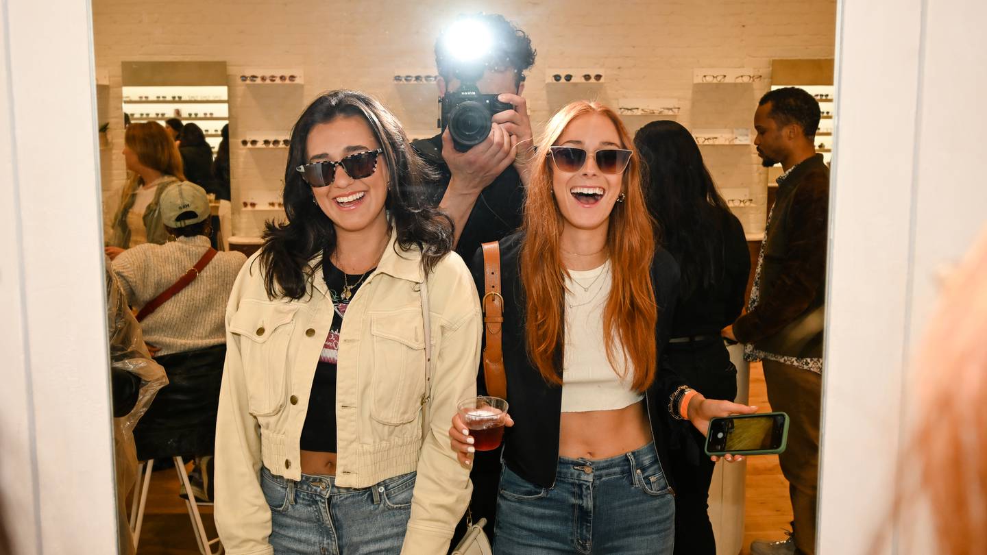 Photographer takes mirror selfie of two girls in a sunglasses store.
