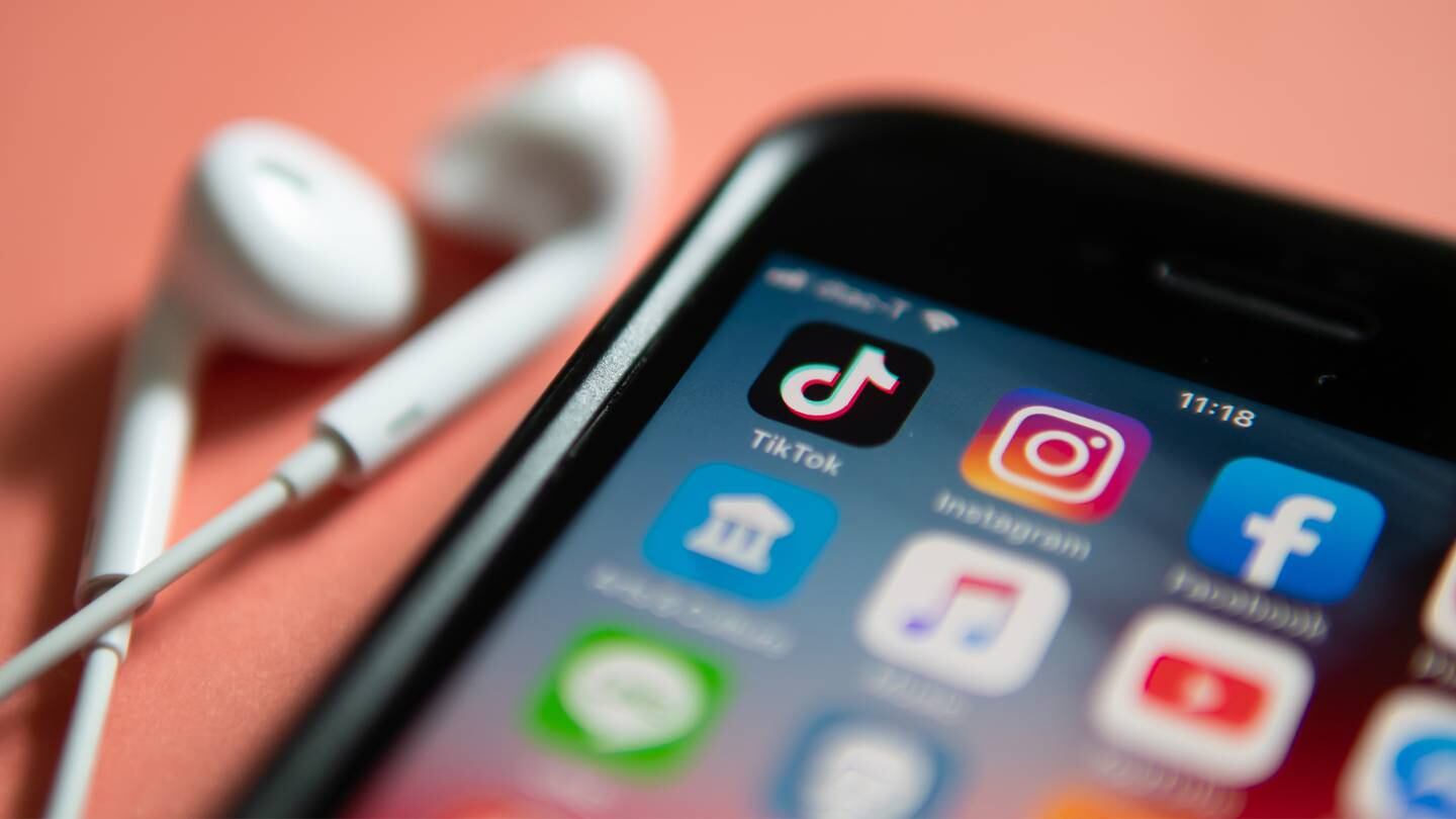 An IPhone displaying app icons, with the TikTok and Instagram app icons in focus in the centre of the image. Headphones lie to the left of the phone.