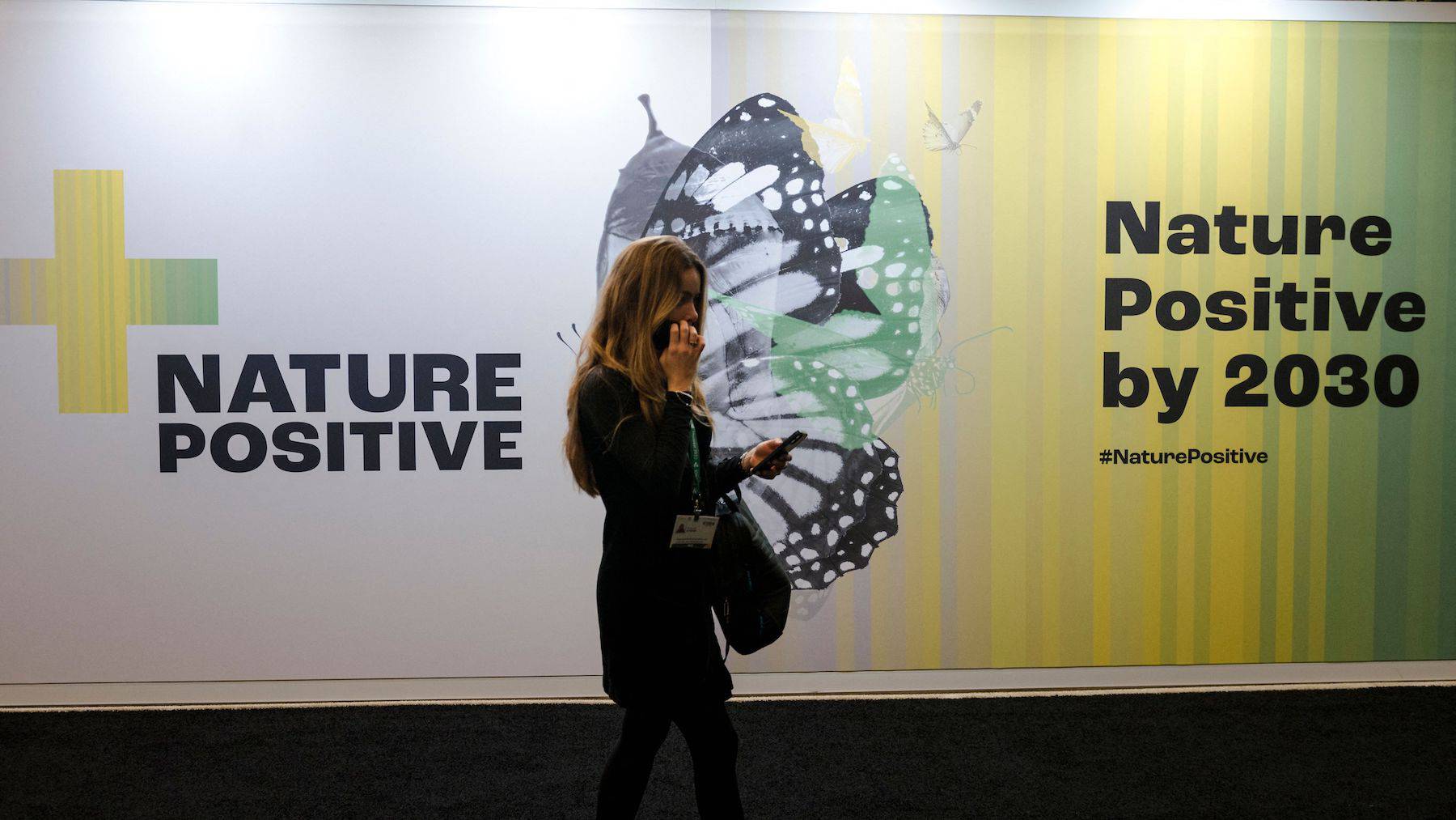 A delegate walks by a sign saying "Nature Positive by 2030" at the United Nations Biodiversity Conference (COP15).