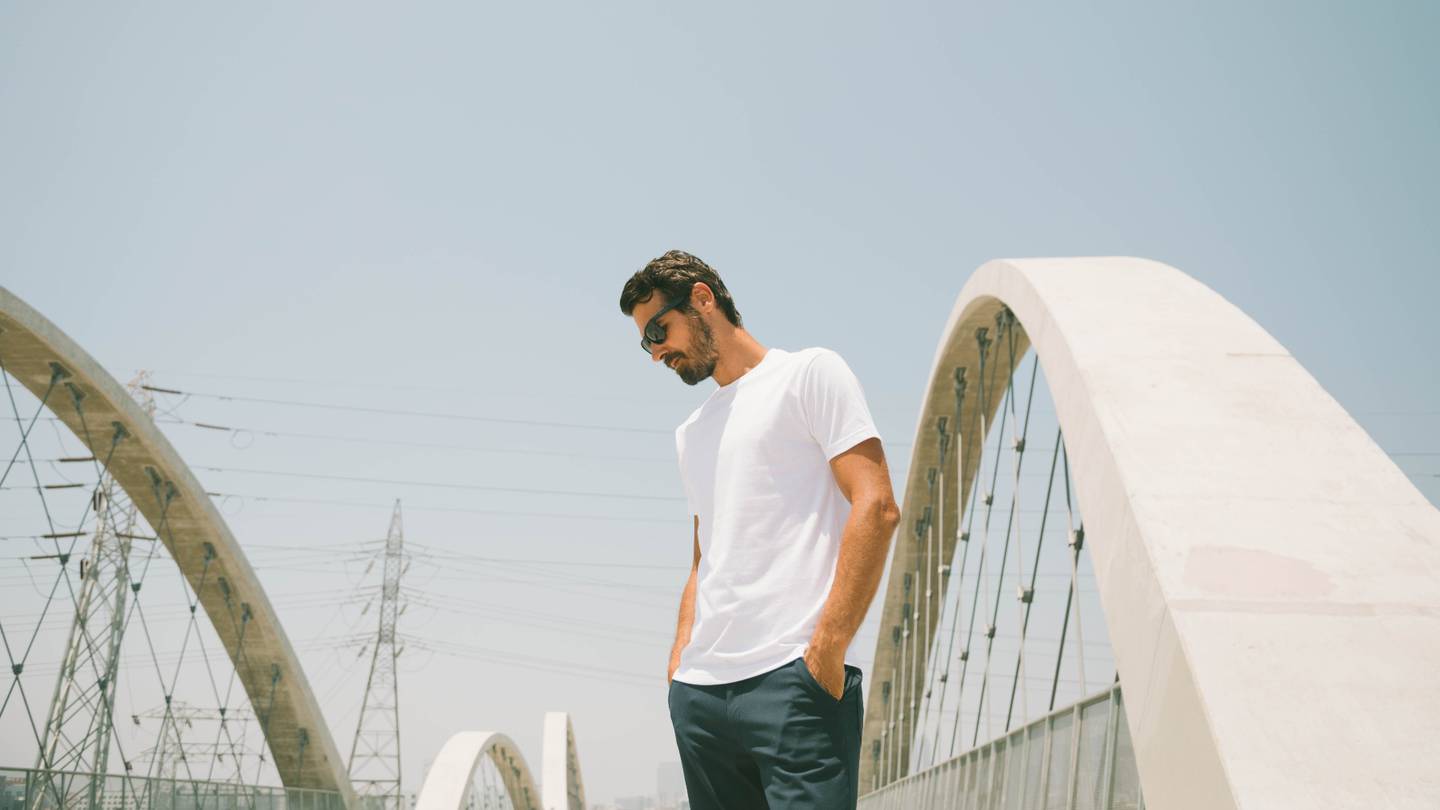 A man poses on a bridge wearing a True Classic t-shirt