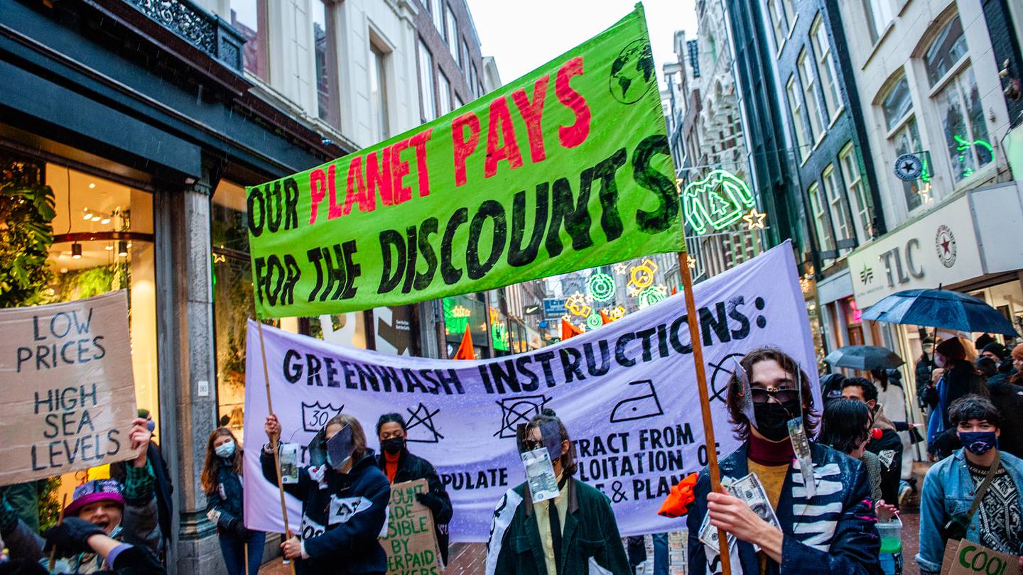 Extinction Rebellion activists march in a demonstration against fast fashion in Amsterdam, holding a green banner that says "our planet pays for the discounts."