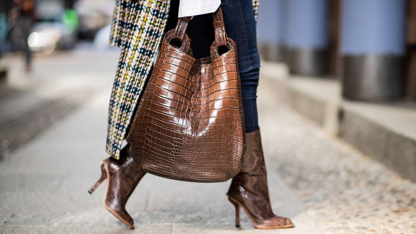 A Milan Fashion Week guest wearing brown python boots and oversize crocodile leather bag in September 2018.