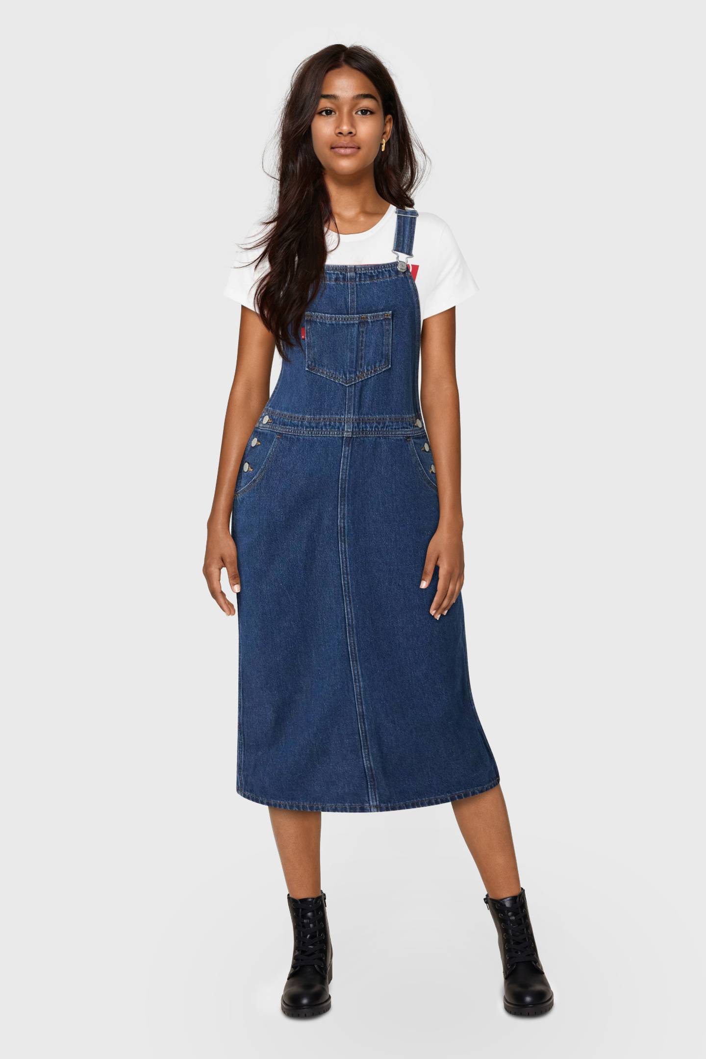 A realistic-looking young female model wears Levi's overalls and looks into the camera.