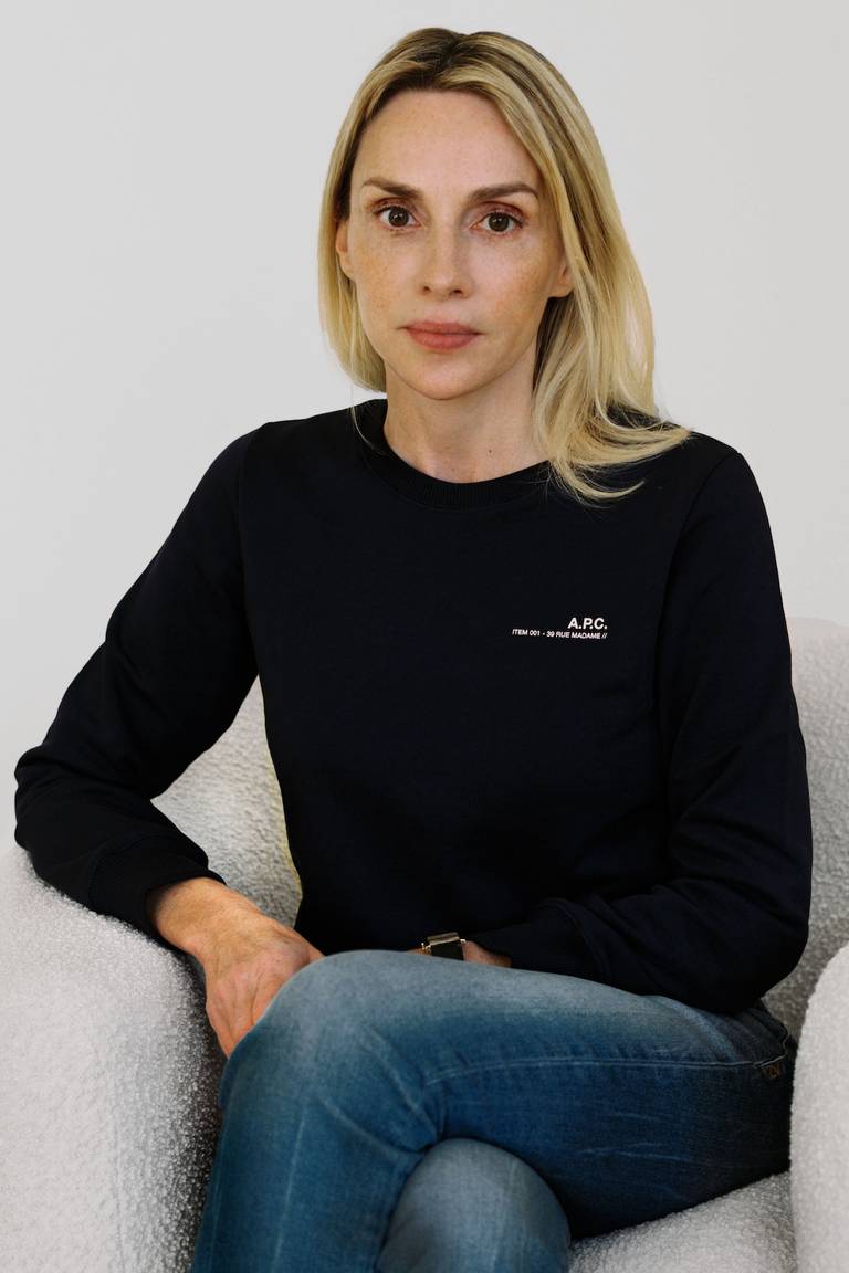 Invisible Collection co-founder Isabelle Dubern-Mallevays sits in an armchair, wearing a black jumper and blue denim jeans.