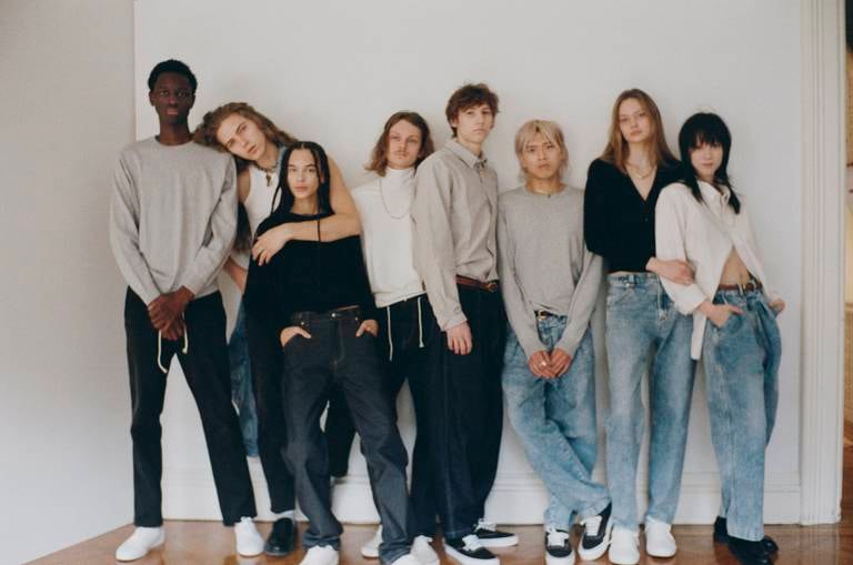 A group of models in jeans standing carelessly against a white wall.